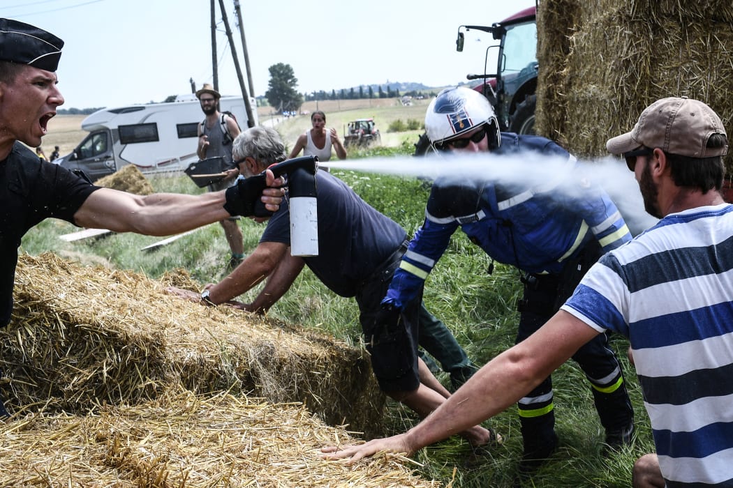 A gendarme (L) sprays tear gas at protesters (R, some hidden) as other gendarmes remove haystacks from the route, during a farmers' protest who attempted to block the stage's route, during the 16th stage of the 105th edition of the Tour de France cycling race.