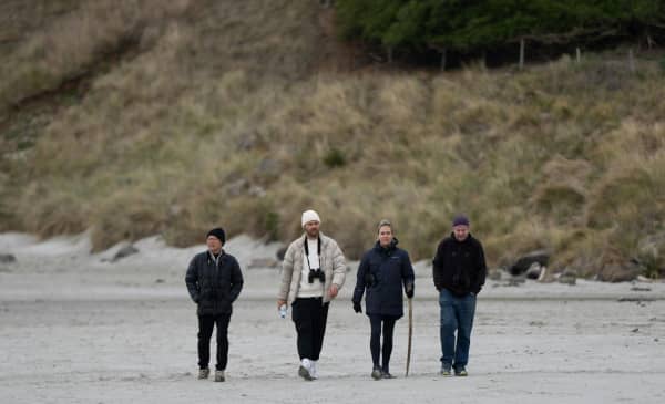 A group of four people walk side by side on a beach.