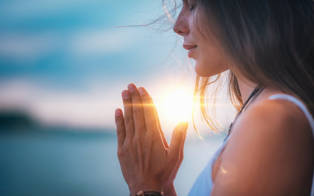 Young woman meditating with her eyes closed, practicing Yoga with hands in prayer position.