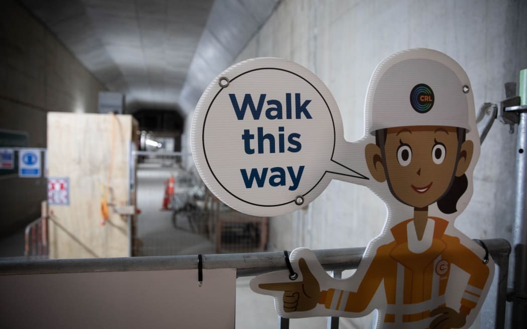 A sign that shows a woman saying "walk this way", while construction equipment is visible in the background.