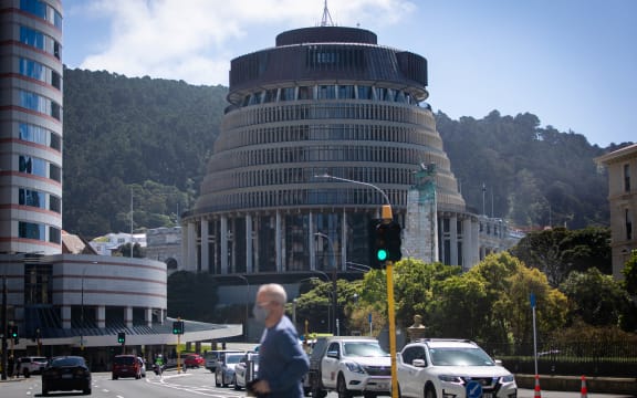 A man wearing a mask crosses the street in front of Parliament