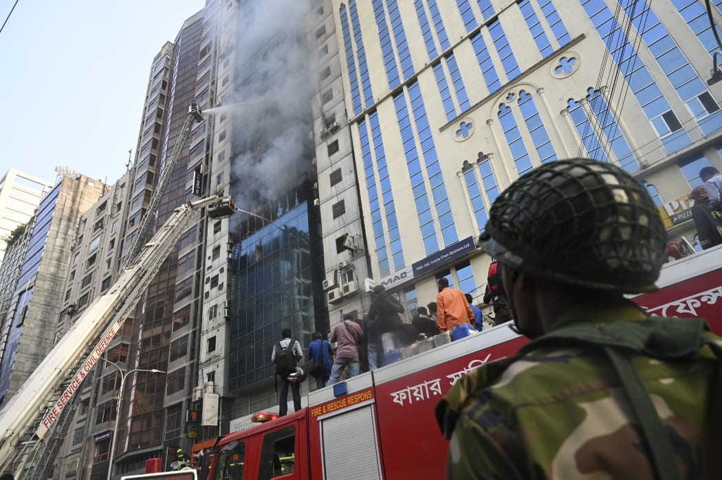A Bangladehi Army stnad guard as Bangladeshi firefighters on ladders work to extinguish a blaze in Dhaka.