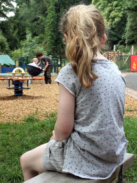 A photo of a lonely girl at the playground watching other kids playing.