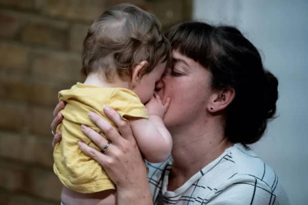 A brown-haired mum kisses her baby who is wearing a yellow t-shirt.