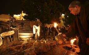 A priest places a candle in front of an installation depicting the nativity of Christ with a figure "symbolizing baby Jesus lying in his manger amid rubble", in reference to Gaza, is displayed in front of the Church of the Nativity in the city of Bethlehem in the occupied West Bank on December 23, 2023. (Photo by HAZEM BADER / AFP)