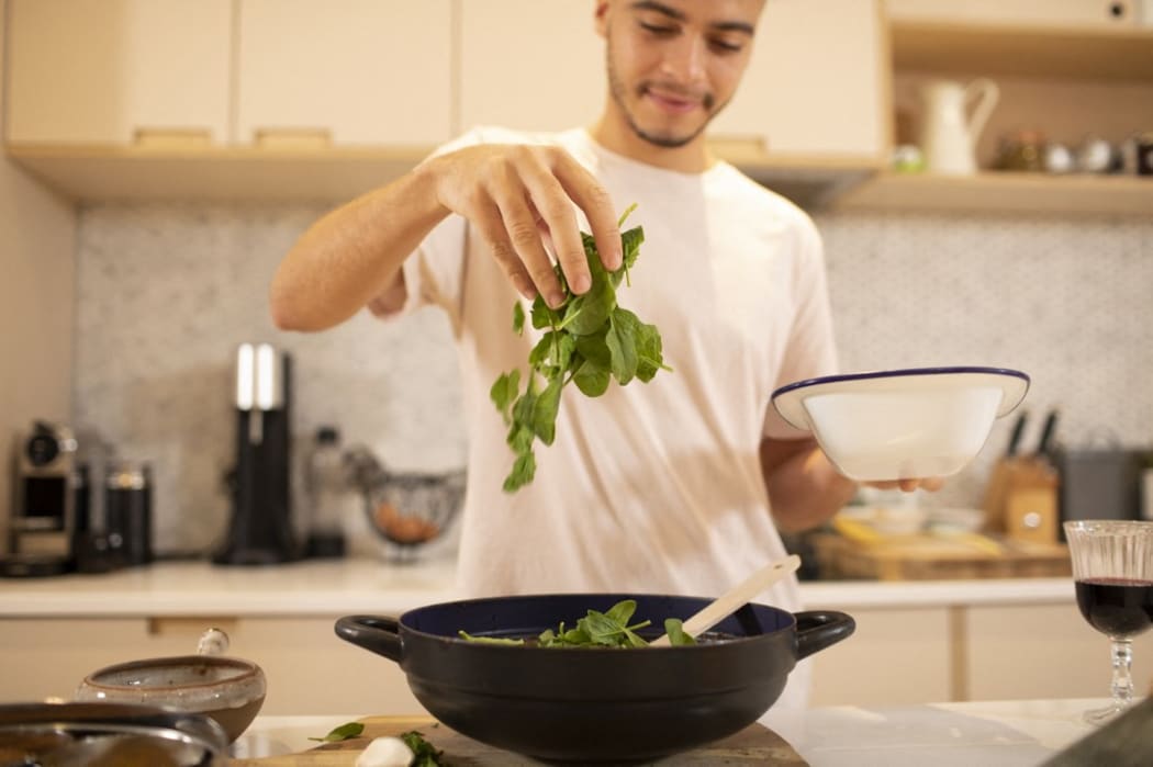 Young man cooking with fresh spinach in kitchen. (Photo by Sam Edwards/CAIA IMAGE/SCIENCE P / NEW / Science Photo Library via AFP)