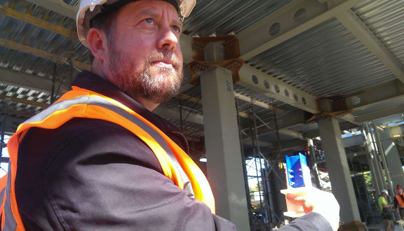 Greg MacRae with a prototype of the sliding joint technology being used in the building behind him.