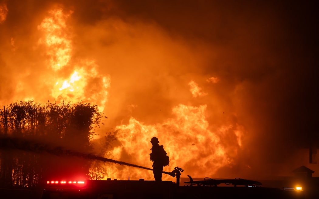 LOS ANGELES, CALIFORNIA - JANUARY 8: A firefighter stands on top of a fire truck to battle the Palisades Fire while it burns homes on the Pacific Coast Highway amid a powerful windstorm on January 8, 2025 in Los Angeles, California. The fast-moving wildfire has grown to more than 2900-acres and is threatening homes in the coastal neighborhood amid intense Santa Ana Winds and dry conditions in Southern California.   Apu Gomes/Getty Images/AFP (Photo by Apu Gomes / GETTY IMAGES NORTH AMERICA / Getty Images via AFP)