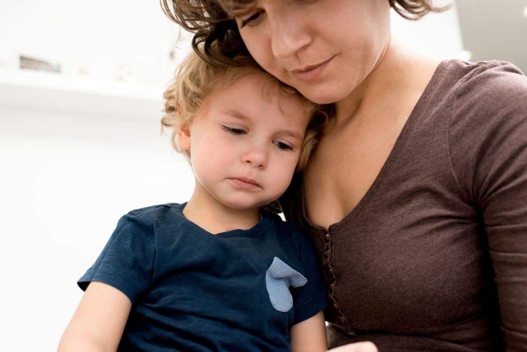 Close up portrait of a cute little boy crying on mothers lap after being scared