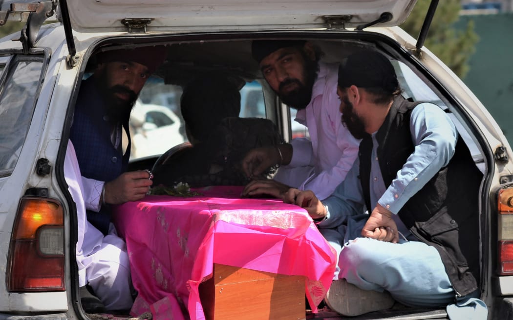 People travel in the back of car with the coffin of a victim following an attack by gunmen at a Sikh temple in Kabul on 18 June.