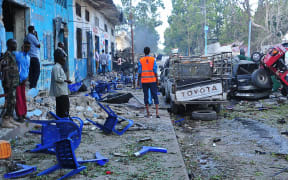 People stand among damages at the scene of a blast after two car bombs exploded in Mogadishu on October 28, 2017.