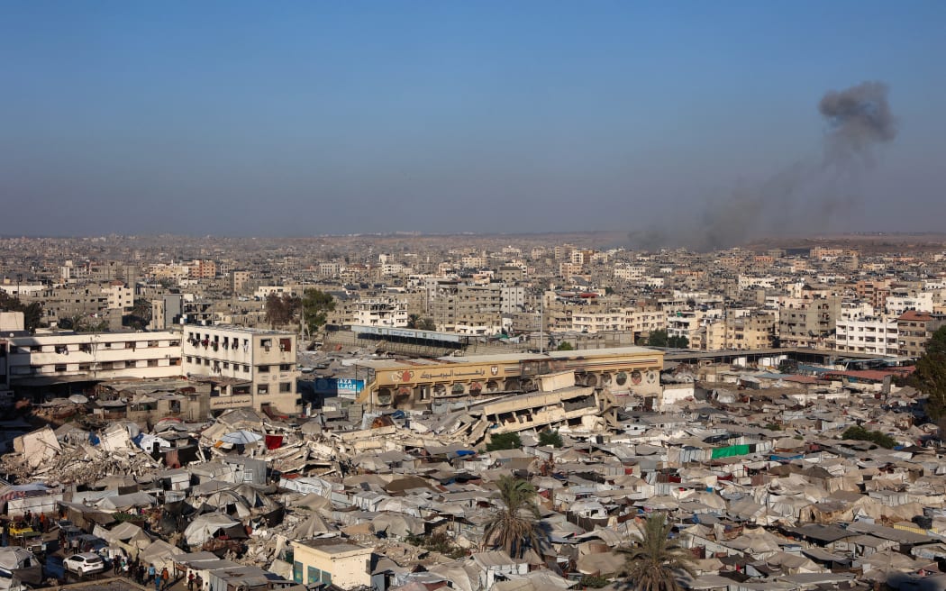 A picture shows a view of a makeshift displacement camp at the Yarmuk Sports Stadium, once a football arena, as smoke billows during Israeli strikes on Gaza City on September 4, 2025. (Photo by Omar AL-QATTAA / AFP)