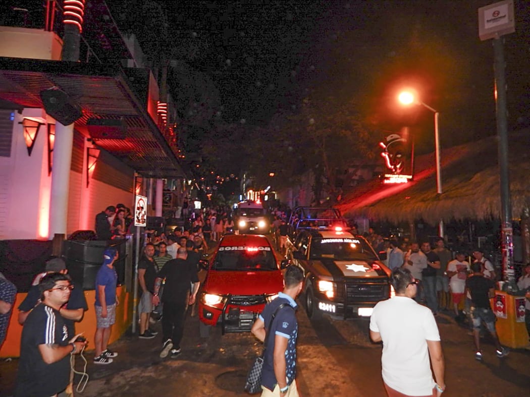 People remain in the street outside the Blue Parrot nightclub as firefighters and police agents patrol the area in Playa del Carmen, Quintana Roo state, Mexico where 5 people were killed, three of them foreigners, during a music festival on January 16, 2017.