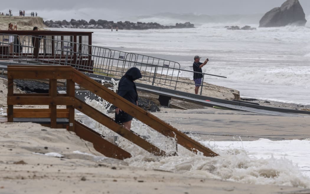 People gather on the beach to watch the large waves generated by Tropical Cyclone Alfred at Currumbin on the Gold Coast on March 6, 2025. The outer fringe of Tropical Cyclone Alfred started whipping eastern Australia on March 6, bringing drenching rains and record-breaking waves to a heavily populated region rarely hit by typhoons. (Photo by David GRAY / AFP)