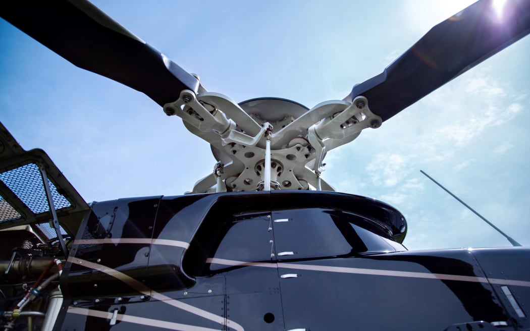 63552730 - close up of a screw of black with gray stripes bell 407 helicopter standing on green grass field in blue sky background.