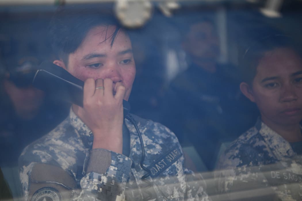 This photo taken on August 22, 2023 shows a female member of the Philippine coast guard issuing a radio challenge to a Chinese coast guard ship during the re-supply mission by a civilian boat chartered by the Philippine navy to deliver supplies to Philippine navy ship BRP Sierra Madre in the disputed South China Sea. A team of AFP journalists on board the BRP Cabra, one of the two Philippine Coast Guard escort boats, watched as one of the Chinese ships came within several meters of the vessel. AFP was one of three media outlets given the rare opportunity to join the Philippine resupply mission to Second Thomas Shoal, less than three weeks after Chinese coast guard ships water cannoned a similar replenishment operation. (Photo by Ted ALJIBE / AFP)