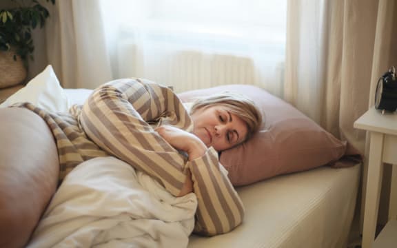 A woman lying down in bed wearing pyjamas and hugging a blanket as she falls asleep.