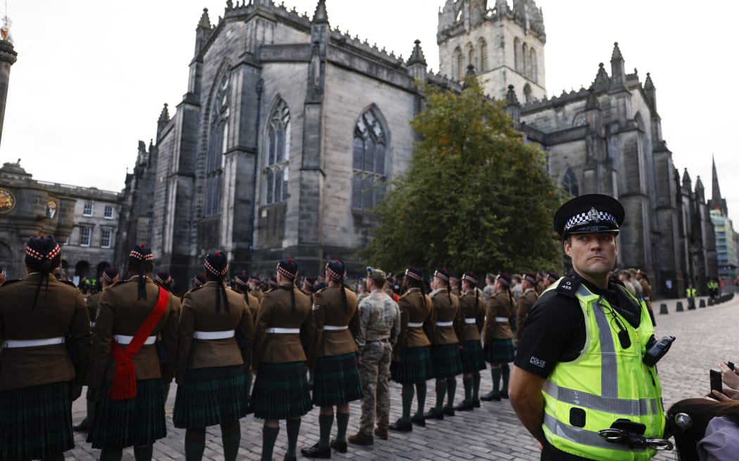 A Police officer stands guard as members of the Royal Regiment of Scotland rehearse on the eve of the Royal Mile outside of St Giles' Cathedral in Edinburgh on September 10, 2022, two days after Queen Elizabeth II died at the age of 96. - King Charles III pledged to follow his mother's example of "lifelong service" in his inaugural address to Britain and the Commonwealth on Friday, after ascending to the throne following the death of Queen Elizabeth II on September 8. (Photo by Odd ANDERSEN / AFP)