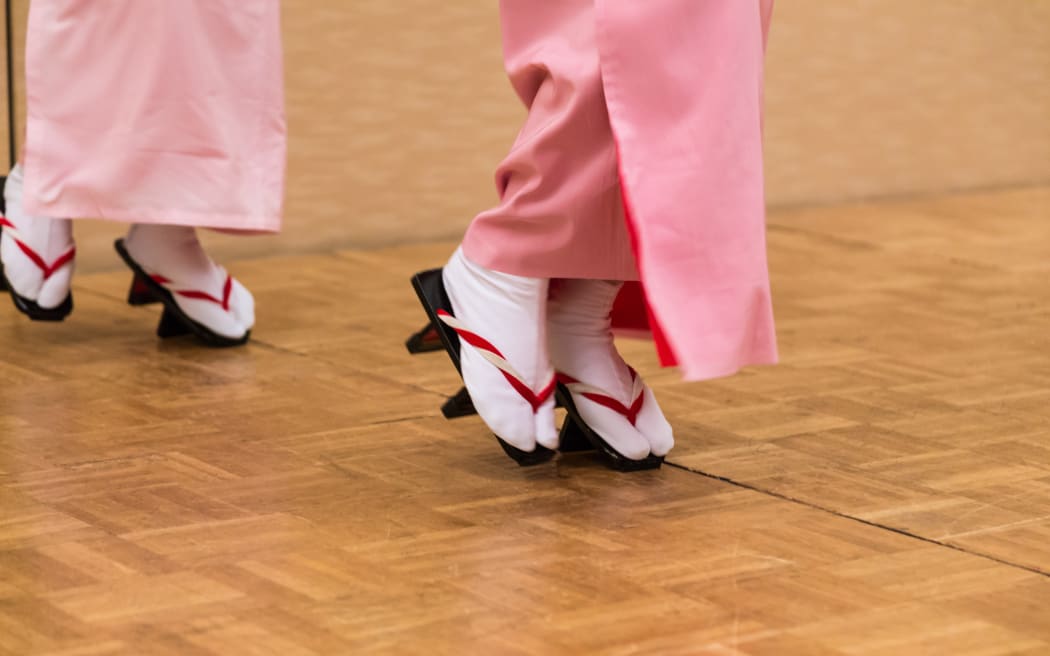View of Japanese women legs and feet in full traditional dress and Japanese style geta shoes, standing and dancing on front part of their shoes.