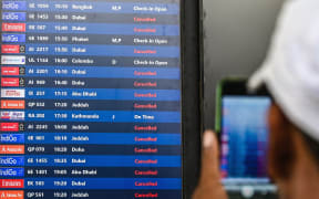 A passenger takes pictures of a flight information board at the Chhatrapati Shivaji Maharaj International Airport in Mumbai on March 1, 2026 after India's two largest private carriers IndiGo and Air India suspended flights to all destinations in the Middle East. Thousands of flights have been delayed or cancelled in the biggest disruption to global air transport since the Covid pandemic as airlines suspend services to the Middle East following the US and Israeli attacks on Iran. (Photo by Punit PARANJPE / AFP)