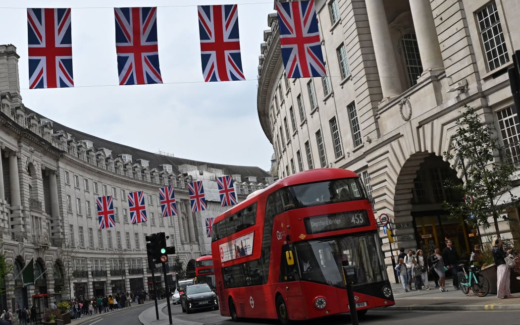 A red London bus passes beneath Union flags on Regent Street, in central London, on April 30, 2023 ahead of the coronation ceremony of Charles III and his wife, Camilla, as King and Queen of the United Kingdom and Commonwealth Realm nations, on May 6, 2023. (Photo by JUSTIN TALLIS / AFP)