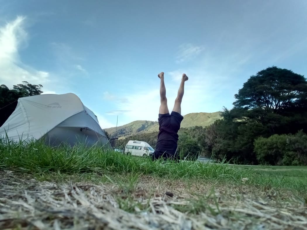 Bruce Hopkins performs a headstand next to his tent.