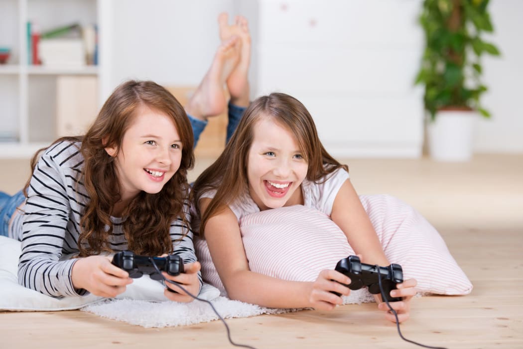 A photo of two young girls happily playing video games in a console laying on the living-room floor