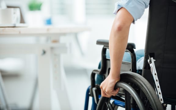 Woman in wheelchair next to an office desk, hand close up, unrecognizable person