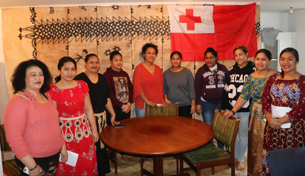Standing in front of a large tapa cloth and a Tongan flag, the nine Tongan women of the night shift gather to support each other.