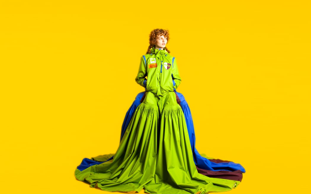 Image of a lime green bustle-style gown with teal blue accents on a vibrant orange-yellow background.