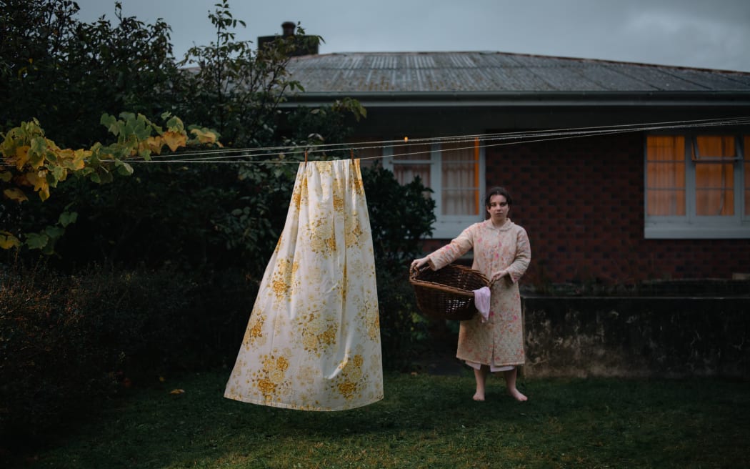 Mary (Maya Le Roux) stands at the clothesline in the rain.
