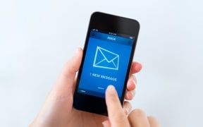 Woman holding phone showing email inbox.