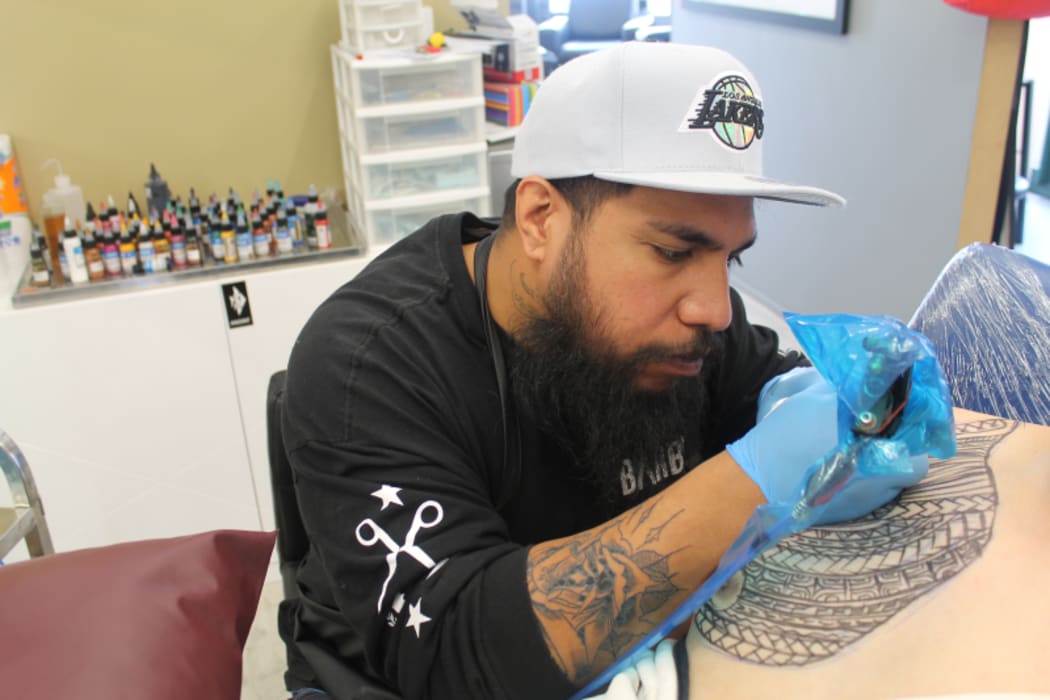An image of tattoo artist, studio owner and art historian Stan Lolohea at work on a large tattoo.