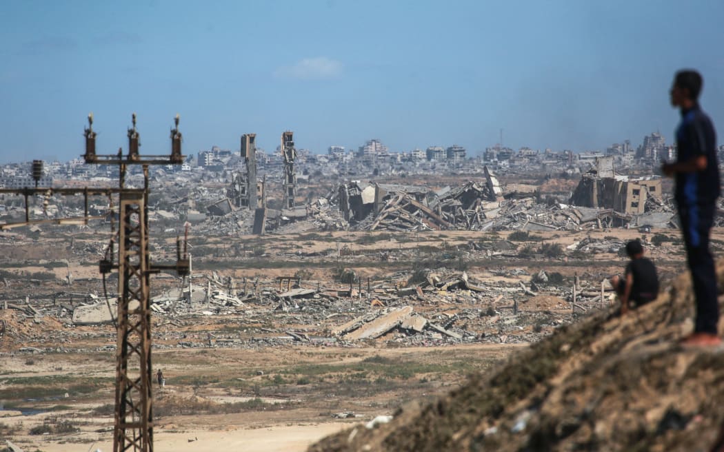 Palestinians watch smoke billowing during Israeli strikes, upon arrival on a coastal path northwest of Nuseirat refugee camp as they are displaced southward from Wadi Gaza following an Israeli announcement of closing Al-Rashid road towards the north of the besieged Gaza Strip on 1 October, 2025.