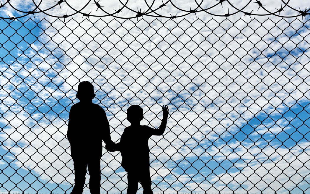 Refugee children concept. Silhouette of two children of refugees near the border fence of barbed wire