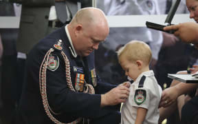 Australian Rural Fire Service Commissioner Shane Fitzsimmons pinning a medal on Geoffrey Keaton's son Harvey.