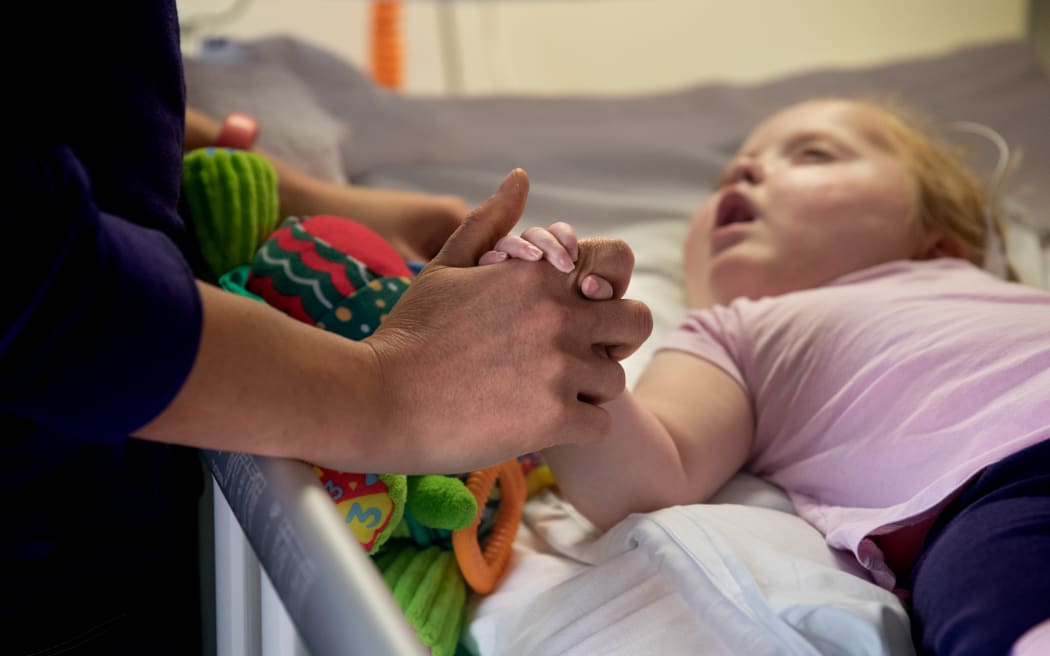 Lauren holds her mothers hand from her bed on the children's ward at Wellington Regional Hospital