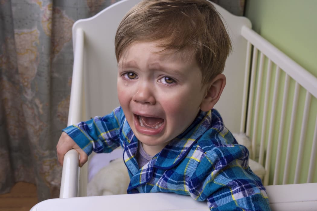 A photo of a small boy having a tantrum at bedtime in his cot