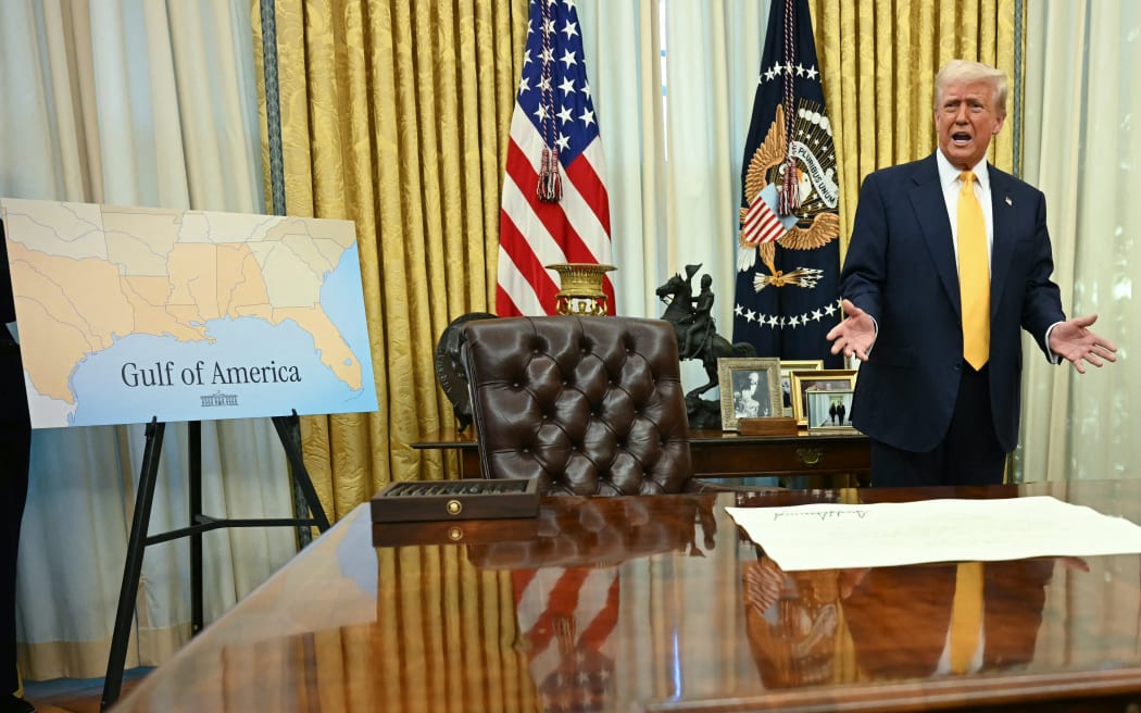 A poster with a map captionned "Gulf of America" is seen as US President Donald Trump stands by the signed commission to make Howard Lutnick US Secretary of Commerce (R) sitting on the Resolute Desk in the Oval Office of the White House in Washington, DC, on February 21, 2025. (Photo by Jim WATSON / AFP)