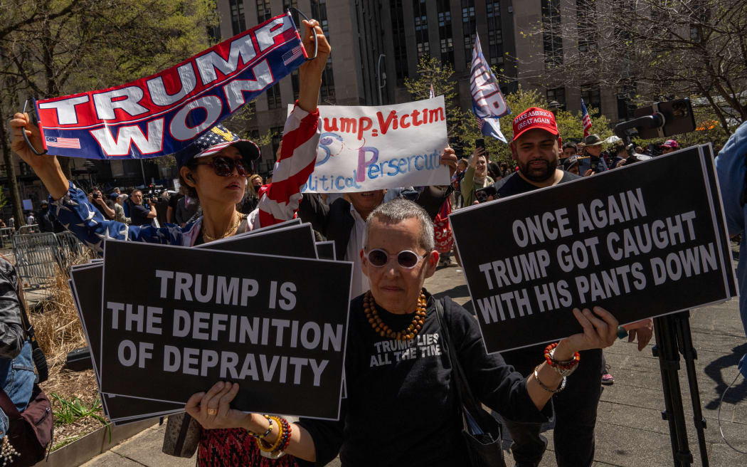 Pro-Trump and anti-Trump demonstrators hold up signs outside of Manhattan Criminal Court as former US President Donald Trump attends the first day of his trial for allegedly covering up hush money payments linked to extramarital affairs, in New York City on April 15, 2024. Trump is in court Monday as the first US ex-president ever to be criminally prosecuted, a seismic moment for the United States as the presumptive Republican nominee campaigns to re-take the White House. The scandal-plagued 77-year-old is accused of falsifying business records in a scheme to cover up an alleged sexual encounter with adult film actress Stormy Daniels to shield his 2016 election campaign from adverse publicity. (Photo by Adam Gray / AFP)