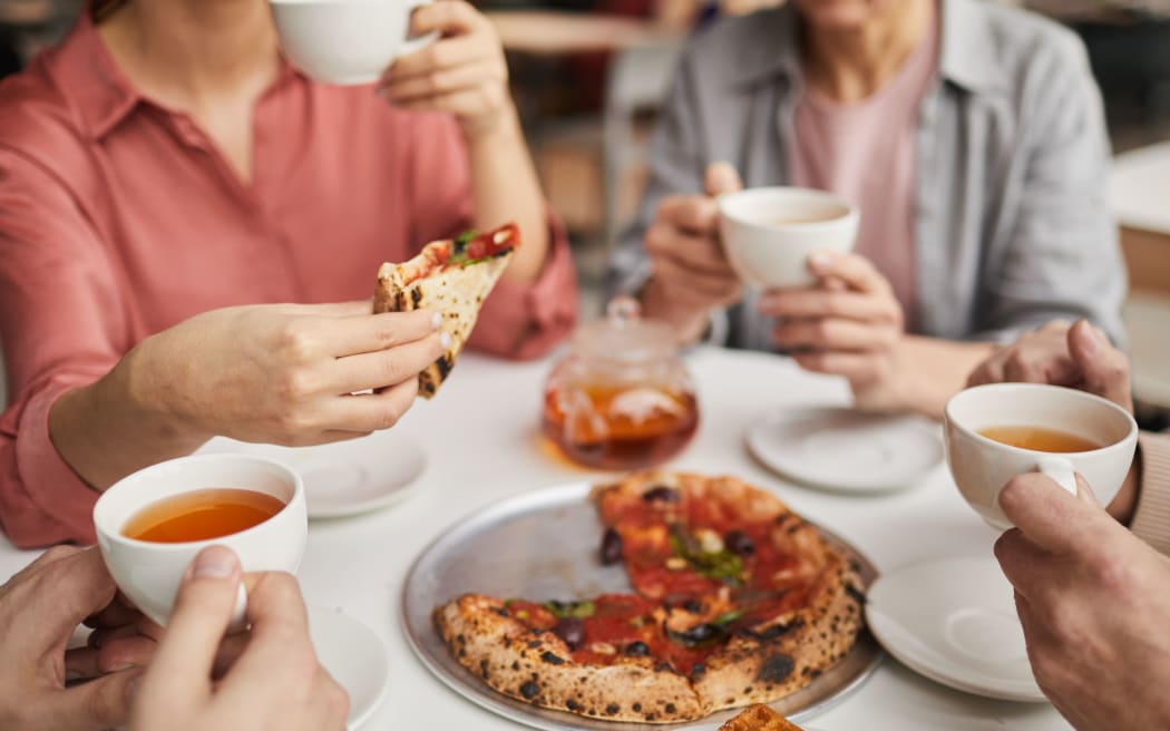 Close-up of woman holding piece of pizza and having lunch together with her family at the table