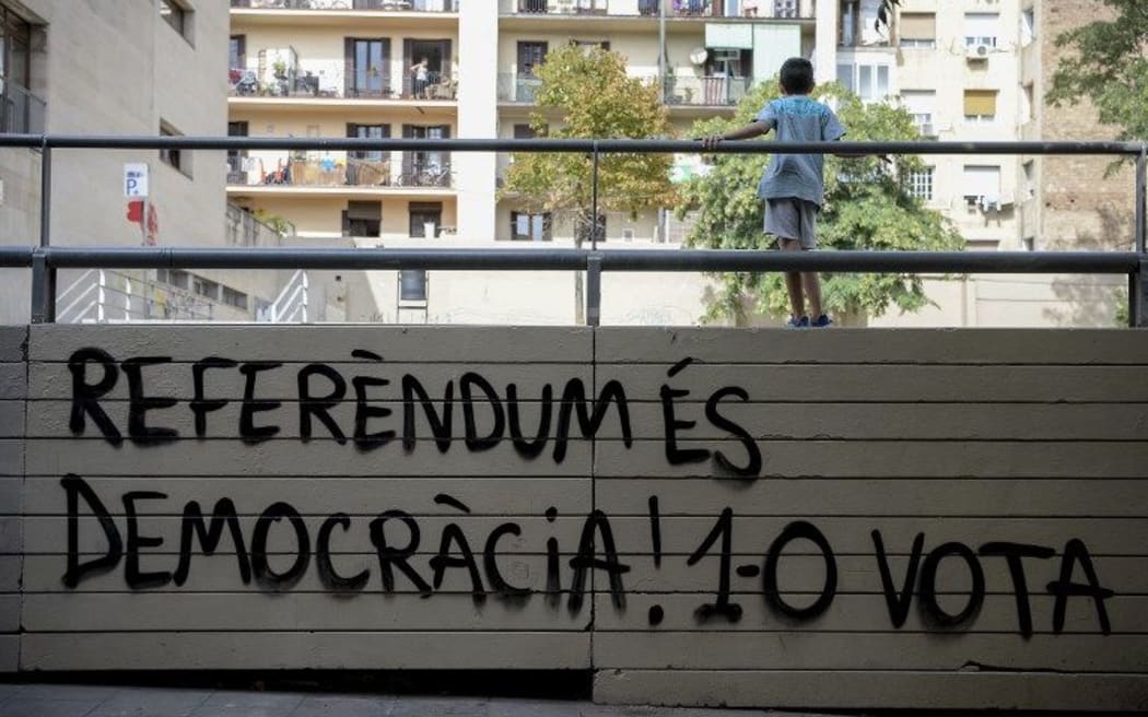 A child stands over a graffiti reading in Catalan "Referendum is democracy! 1-O (October 1) do vote" in Barcelona