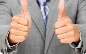 A man wearing a suit puts two thumbs up.