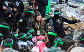 Hamas militants escort Israeli hostage Agam Berger (C) before handing her over to a Red Cross team in Jabalia on January 30, 2025, as part of their third hostage-prisoner exchange. (Photo by Omar AL-QATTAA / AFP)