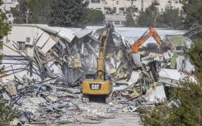 A photograph shows machinery demolishing a structure inside the headquarters of the United Nations Relief and Works Agency (UNRWA) in the Sheikh Jarrah neighbourhood of Israeli-annexed east Jerusalem on January 20, 2026. Israeli bulldozers began demolitions at the headquarters of the UN agency for Palestinian refugees in east Jerusalem on January 20, in what the organisation called an "unprecedented attack". The compound in Israeli-annexed east Jerusalem has been empty of UNRWA staff since January 2025, when a law banning its operations took effect after a months-long battle over its work in the Gaza Strip. (Photo by ILIA YEFIMOVICH / AFP)