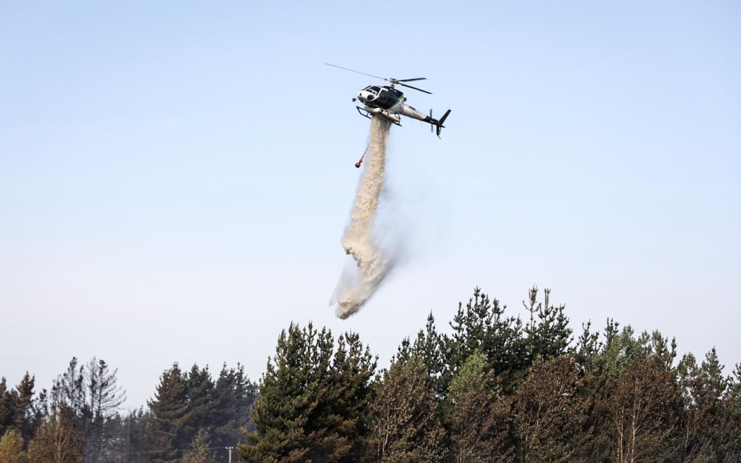Helicopters dropping water on the burning area of trees.