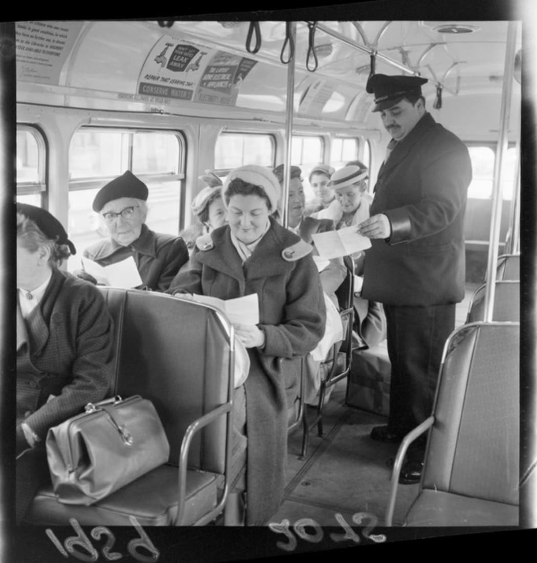 Bus driver Mr D Vasiliu handing out voting forms to passengers. (1959) Negatives of the Evening Post newspaper. (Permission of the Alexander Turnbull Library, Wellington, New Zealand, must be obtained before any re-use of this image.)