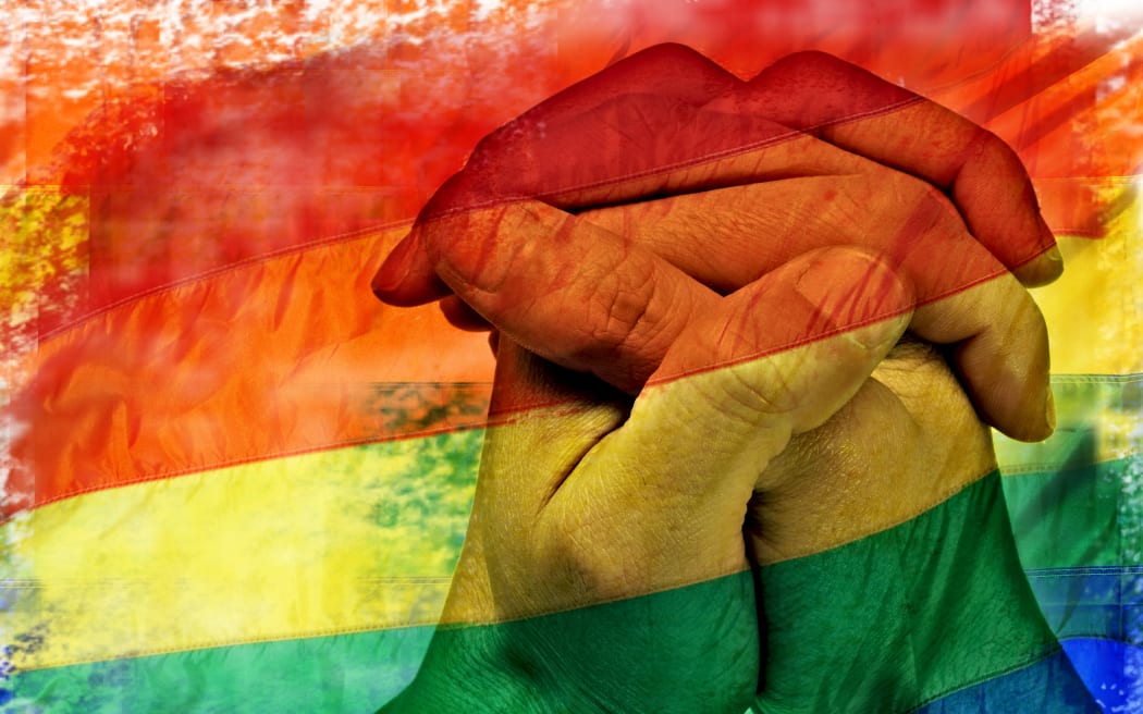 double exposure of a rainbow flag and the hands of a young man put together like praying