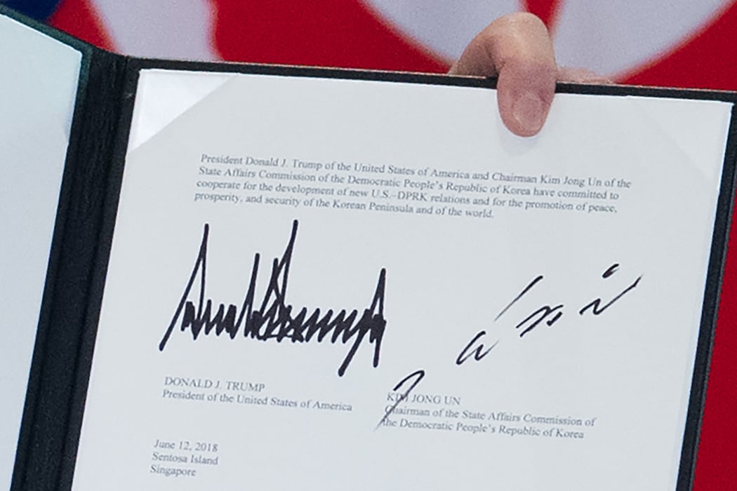 The signatures of US President Donald Trump (L) and North Korea's leader Kim Jong Un (R) are seen on a document held up by Trump following a signing ceremony during their historic US-North Korea summit