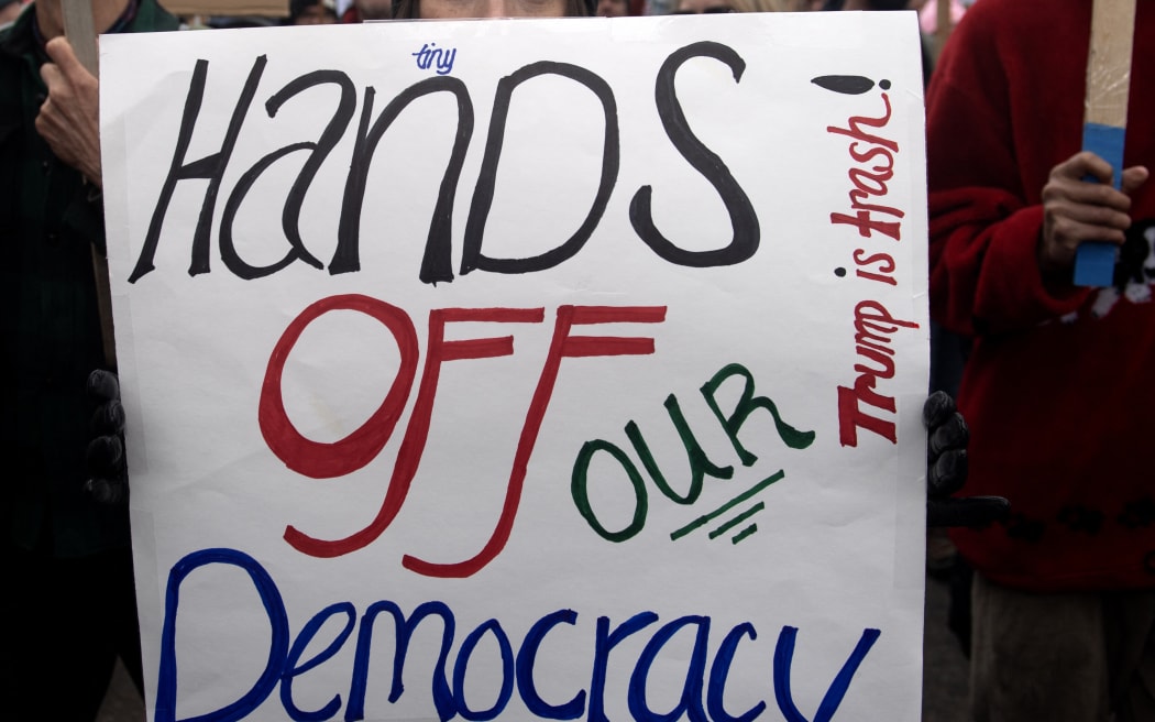 Demonstrators hold up signs during the nationwide 'Hands Off' protest against US President Donald Trump and his advisor, Tesla CEO Elon Musk, at the Colorado Capital in Denver, Colorado on April 5, 2025. Protesters flooded the streets of several major US cities on Saturday to oppose the divisive policies of President Donald Trump, in the largest demonstrations since his return to the White, House. Opponents of the Republican president's policies -- from government staffing cuts to trade tariffs and eroding civil liberties -- rallied in Washington, New York, Houston, Los Angeles and Florida, among other locations. (Photo by Jason Connolly / AFP)